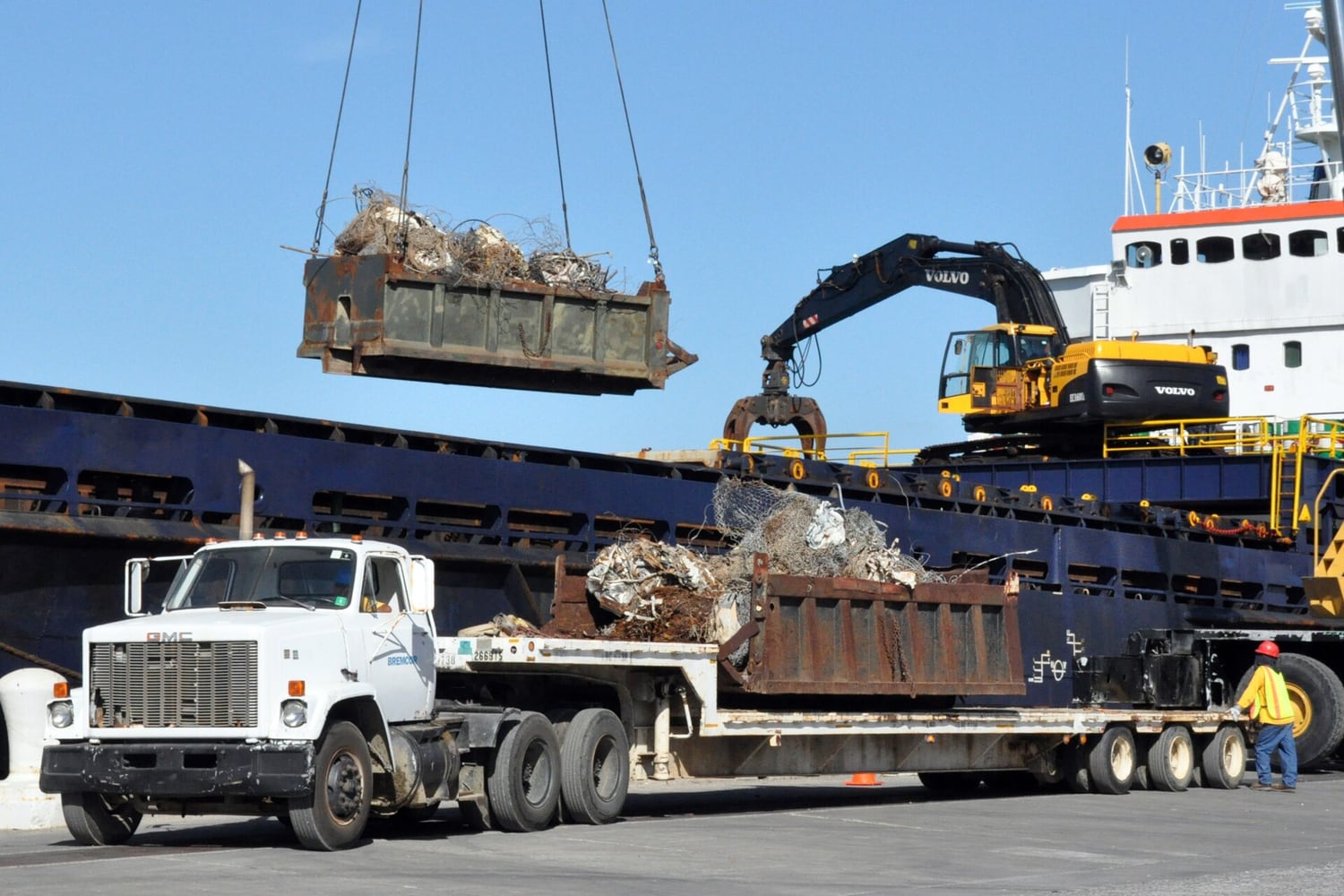Scrap metal lifted from a truck onto a cargo ship by crane